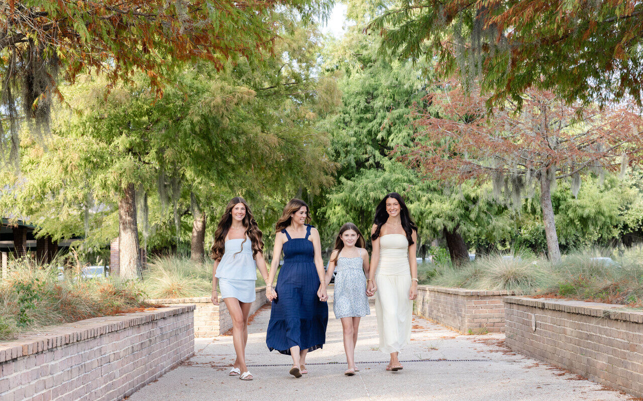 A mother and her three daughters walking together down a tree-lined path